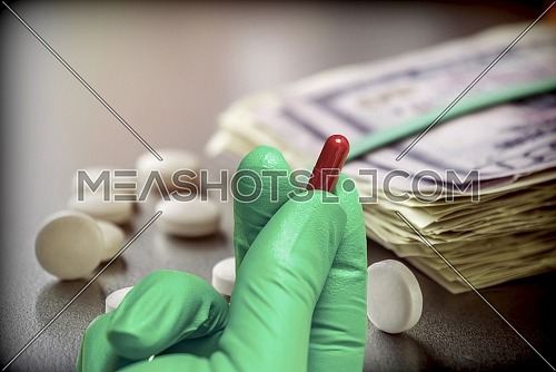 Hand with green glove latex holds red capsule, concept sanitary copayment, conceptual image