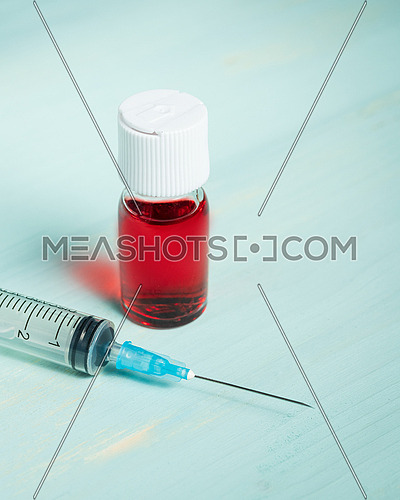 medical vaccine ampule with red liquid and syringe over green table and white background. Vaccination and immunization conceptual.