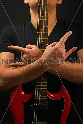 Man holding embracing red sg guitar neck with two hands showing devil horns rock metal sign over black background