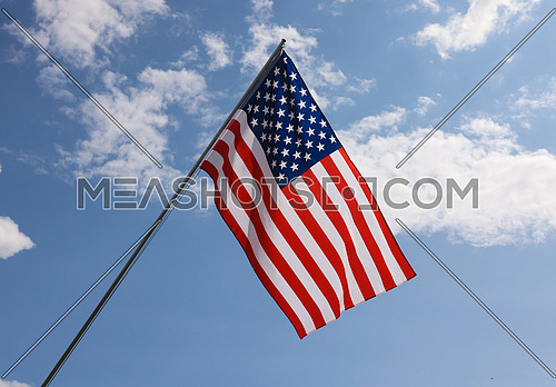 US national flag hanging on flagstaff over cloudy blue sky, symbol of American patriotism, low angle, side view