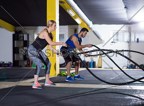 young fit sports couple working out in functional training gym doing crossfitness exercise with battle ropes