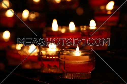 Red glass translucent candles burning in dark church, close up, low angle view
