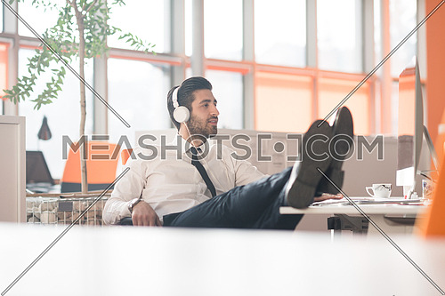 happy young arabian  business man with beard  listening music on headphones at modern startup office
