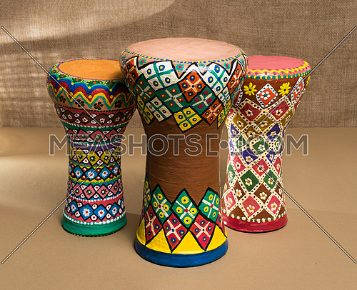 Front view of three decorated colorful pottery goblet drums (chalice drum, tarabuka, darbuka) on background of wooden table, and sackcloth wall