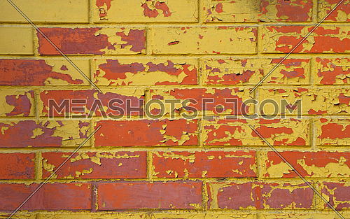 Old grunge red brick wall painted with yellow paint with flakes, stains and defects