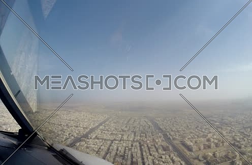 Close shot from inside plane cockpit showing sky horizon from the window and a city at day