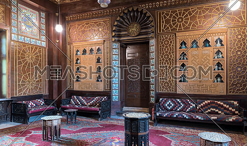 Manial Palace of Prince Mohammed Ali. Guests Hall with wooden ornate ceiling, wooden ornate door, lanterns, colorful ornate couches, tea tables and ornate carpet