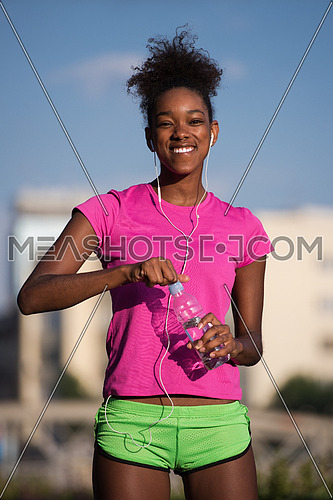 portrait of a young African American girl to run beautiful summer morning on city streets with headphones and a bottle of water