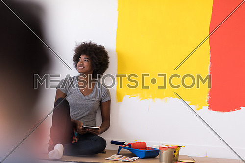 Portrait of a beautiful african american female painter sitting on floor near wall after painting.