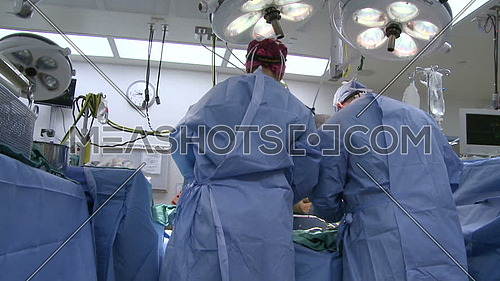 Tilt Down long shot of operating room while medical team performing surgery from behind
