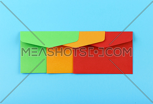 Close up group of three colorful mail envelopes, green, yellow and red, over pastel blue paper background, elevated top view, directly above