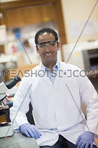 portrait of a young middle eastern man with a microscope in a large modern laboratories