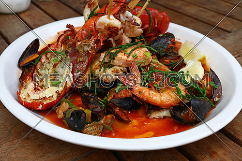 Close up large grilled seafood platter on wooden table, high angle view