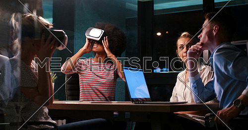 Multiethnic Business team using virtual reality headset in night office meeting  Developers meeting with virtual reality simulator around table in creative office.