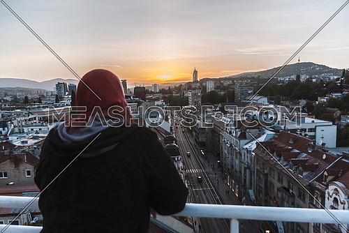 Muslim woman in hijab looking sunset sky on city landscape
