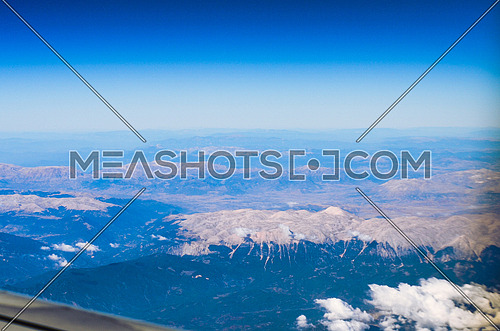 Clear blue sky with clouds and top of the mountains appears underneath and among the clouds