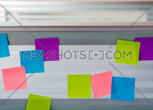 Randomly scattered blank colored sticky notes over glass screen of a bench desk