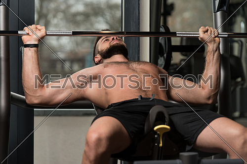 Handsome Man Is Working Out Chest With Barbell In A Modern Gym