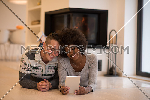 beautiful young multiethnic couple using tablet computer on the floor of their luxury home in front of fireplace at autumn day