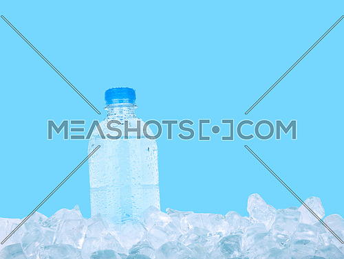 One full PET plastic bottle of cold still drinking water chilling on ice cubes isolated on blue background, low angle side view