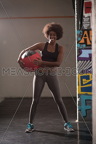 portrait of a young beautiful African American women carrying crossfit ball in gym