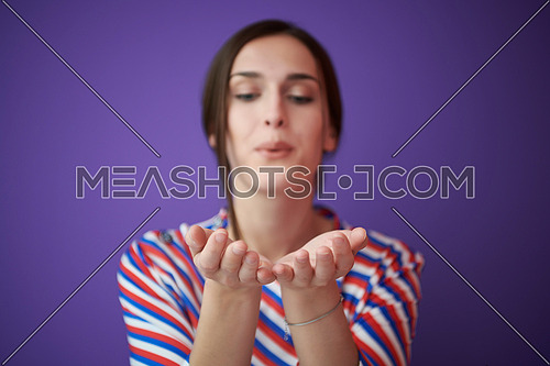 Close up portrait of charrming girl  blowing air kiss from open palm,expresses her devotion and truthful love to boyfriend, isolated on purple background. Modern fashionable girl posing in the studio