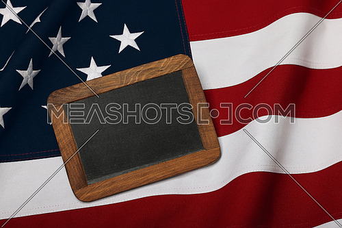 Close up old vintage slate chalk board sign in wooden frame on cotton embroidered US national flag background, symbol of American patriotism, elevated high angle view, directly above