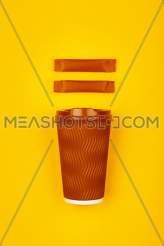 Close up one crimped disposable brown paper takeaway cup and two sugar stick sachet over vivid yellow background, flat lay, elevated top view, directly above