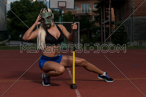 Portrait Of A Physically Fit Young Woman With Hammer And Gas Mask