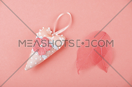 Pink small toy textile heart and two skeleton leaves over design paper background