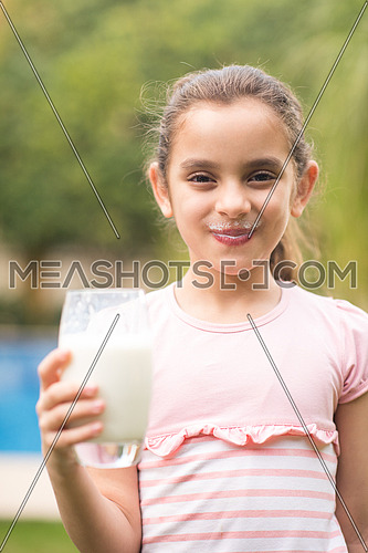 Middle Eastern girl enjoying with a glass of milk in her hand outside on summer day