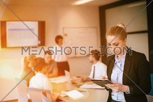businesswoman on meeting using tablet computer  blured group of business people in background at  modern bright startup office interior