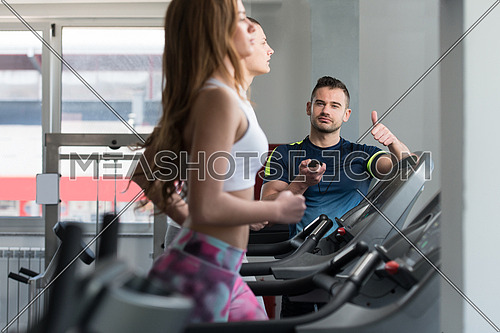 Personal Trainer Showing Ok Sign To Client - Group Of People Exercising On Treadmills In Gym Or Fitness Club