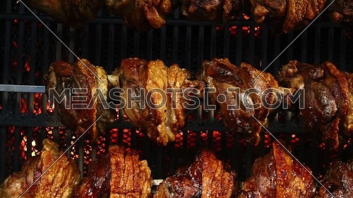 Several traditional Bavarian German roasted pork knuckles slowly cooked at rotating broiling rack grill spit, close up, low angle side view