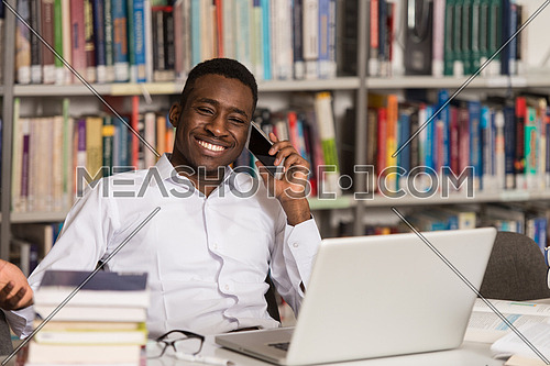 African Male Student Talking On The Phone In Library - Shallow Depth Of Field