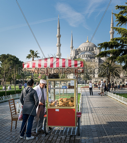 Istanbul, Turkey - April 16, 2017: Tourist buying fast food meal from a traditional Turkish Simit (Bagel) cart with Blue Square in the background
