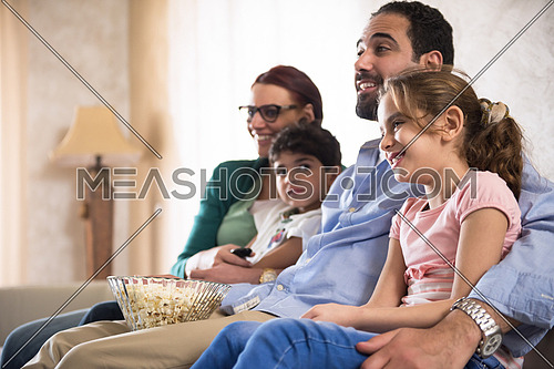 happy middle eastern family enjoys spending a quality time with the kids on the sofa with movies and popcorn