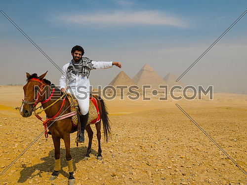 young  Egyptian   man riding arabian horse in desert,  giza platou with grand pyramids in background