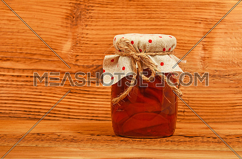 One glass jar of homemade quince jam with textile top decoration at unpainted brown vintage wood