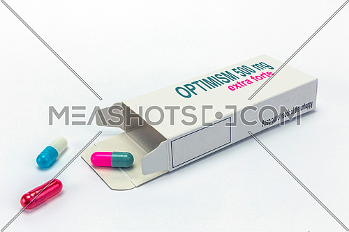 Open medicine packet labelled optimism opened at one end to display a blister pack of tablets, isolated on white