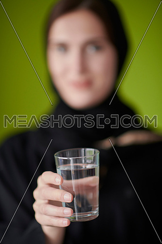 Modern muslim woman in abaya holding a glass of water in front of her. Arab girl representing iftar time, Ramadan kareem concept