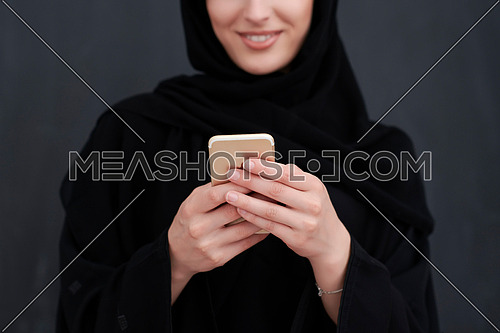 Young muslim businesswoman in traditional clothes or abaya using smartphone. Arab woman standing in front of black chalkboard and representing techology, islamic  fashion and Ramadan kareem concept