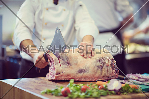 chef using ax while cutting big piece of beef  on wooden board in restaurant kitchen