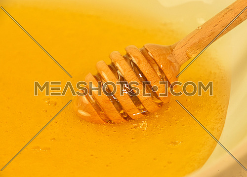 Close up wooden honey dipper spoon in bowl of fresh thick fluid acacia honey, high angle view