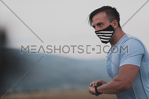 Fitness man in wet sporty clothes wearing black protective face mask running outdoors in the city during coronavirus outbreak. Covid 19 and physical jogging activity, sport and fitness. New normal