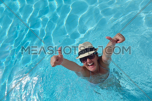 Happy smiling woman with hat and sunglasses  in swimming pool at tropical resort