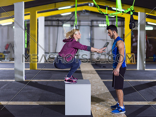 young athletic woman training with personal trainer  jumping on fit box at crossfitness gym