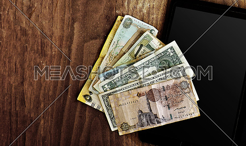different currencies on wood background and tablet