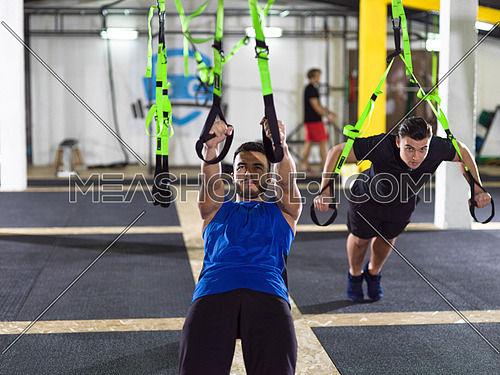 two young athlete men working out pull ups with gymnastic rings at the crossfitness gym