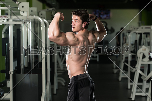 Young Man Standing Strong In The Gym And Flexing Rear Double Biceps Pose - Muscular Athletic Bodybuilder Fitness Model Posing Exercises